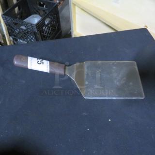 Stainless steel hamburger turner with dark brown handle and label indicating item 45. Slight wear visible.