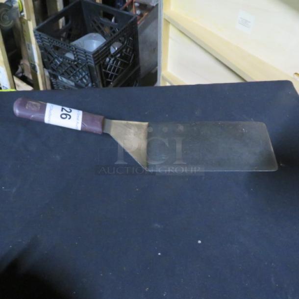 Metal hamburger turner with a maroon handle, light wear, rectangular blade. Features a label with the number 26.