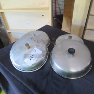 One lot of four metal pot lids on black surface; two have textured handles, one has auction tag "241." Good used condition.