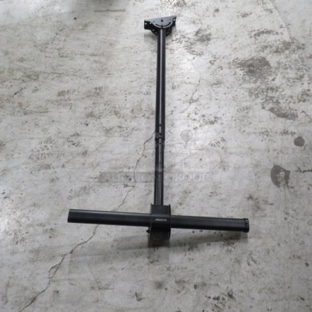 Metal TV mount on concrete floor, black, adjustable arm, mounting bracket on top. Appears new with robust construction.