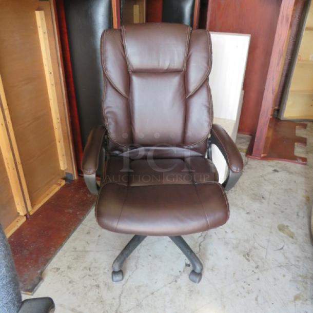 Brown leather executive office chair on casters, featuring padded seat and backrest, adjustable armrests, excellent condition.