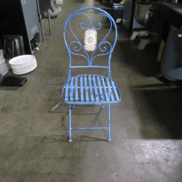 Blue metal folding chair with decorative backrest, showing signs of wear. Suitable for indoor or outdoor use.