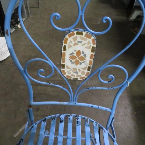 Blue metal folding chair with decorative mosaic backrest, ornate scrollwork. Visible wear and rust on edges.