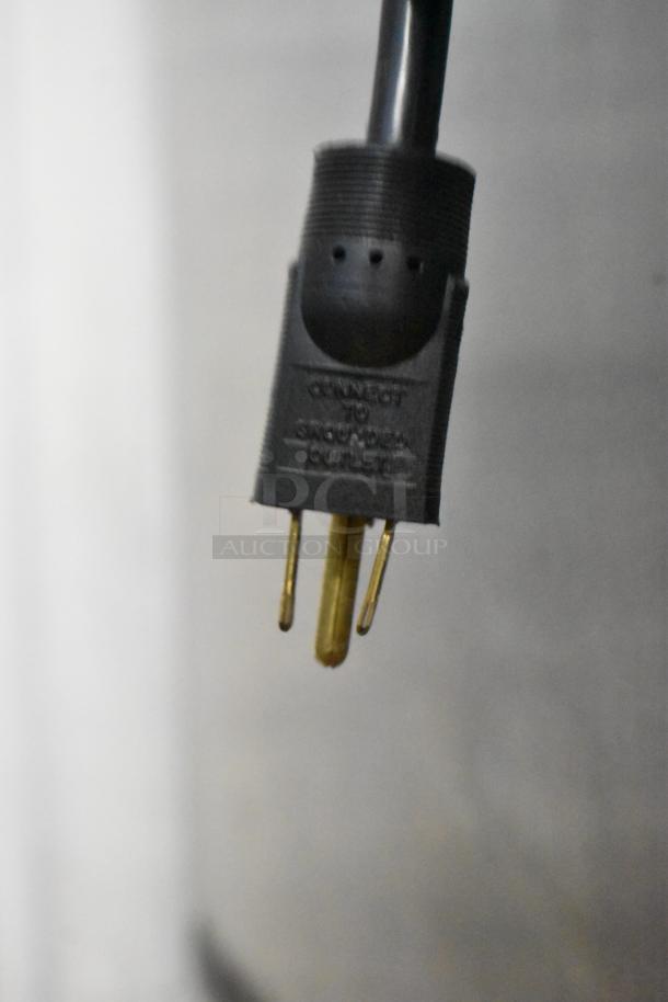 Black plug with three prongs labeled "CONNECT TO GROUNDED OUTLET" seen in a commercial kitchen setting.