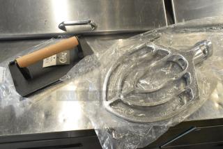 Brand new scratch and dent Choice 9" x 5" cast iron steak weight with wooden handle and commercial dough mixer paddle.