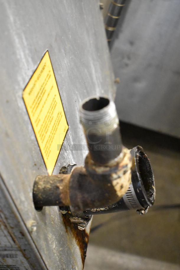 Rusty pipe connection on the back of a gas-powered appliance with a warning label visible.