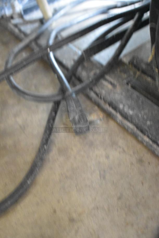 Blurry image showing floor with tangled electrical cords and a plug. No visible details of the cooler merchandiser.
