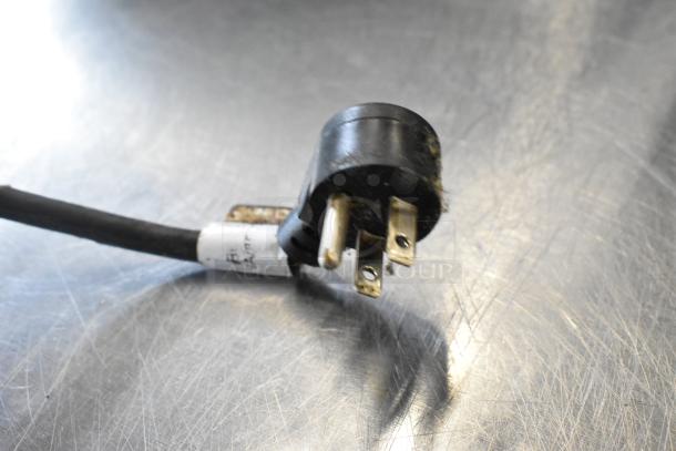 Close-up of a Delfield UCD4464N-12-DD5 stainless steel prep table power plug. Black plug, three prongs, labeled with voltage info.