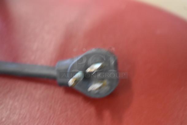 Blurry close-up of a plug, detached from a Migali CA-4-12 stainless steel sandwich salad prep table. Missing lid.