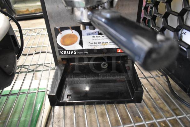 Krups XP524 Espresso Machine with portafilter, shown on a metal shelf. Features "Precise Tamp" labeling. 120V, 1 phase.