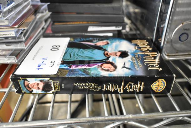 Lot of various DVDs on shelf, including "Harry Potter and the Prisoner of Azkaban" with visible wear. Label indicates 80 quantity, V-lot.