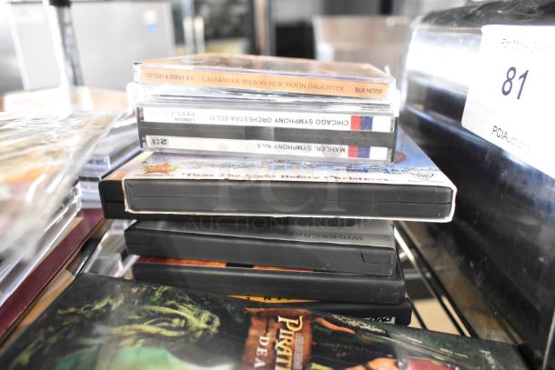 Various DVDs stacked, featuring titles like "Pirates of the Caribbean" and "Twas the Night Before Christmas," in used condition.