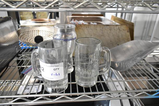 A lot including glass mugs, a glass with blue rim, and a metal ice scoop on a metal shelf, labeled for auction.