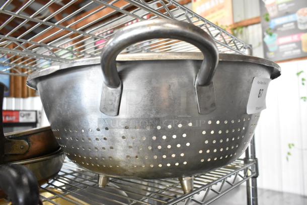 Metal colander with large handles, used condition, perforated design. Includes six other metal items like skillets. Lot labeled 87.