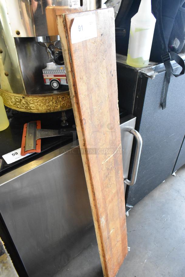 Wooden butcher block cutting board, long and rectangular, showing signs of wear. Features visible grain and texture.