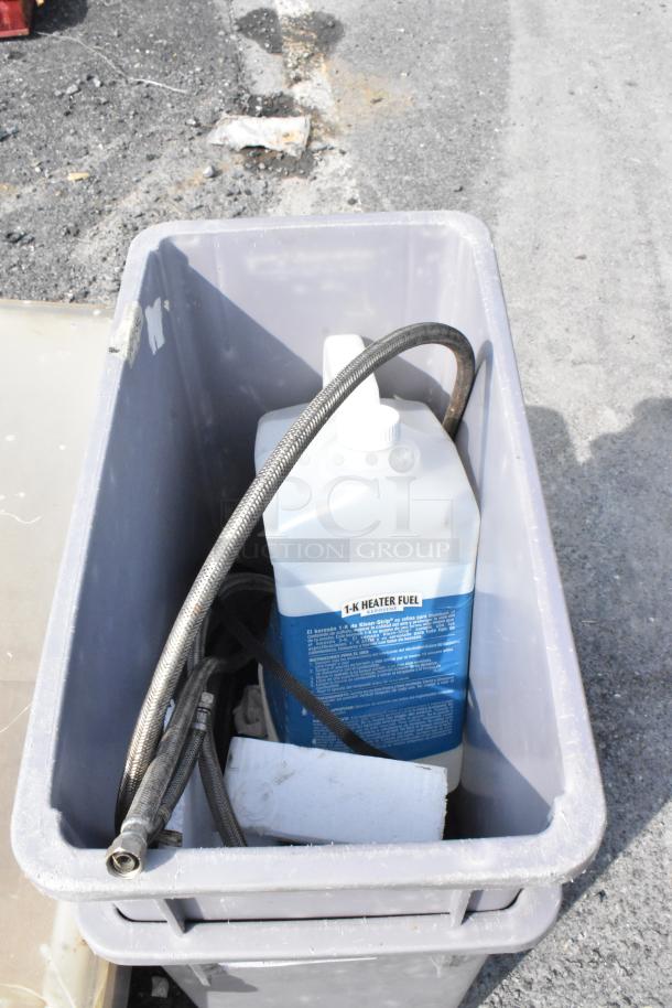 Gray poly trash can with contents including a 1-K heater fuel container and hoses, brand new with minor scratches.