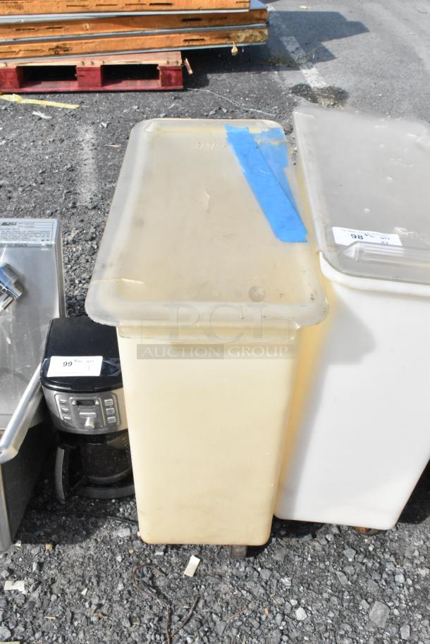 2 white poly ingredient bins on commercial casters, used. Lid has blue tape; tags show lot numbers 98 and 99.