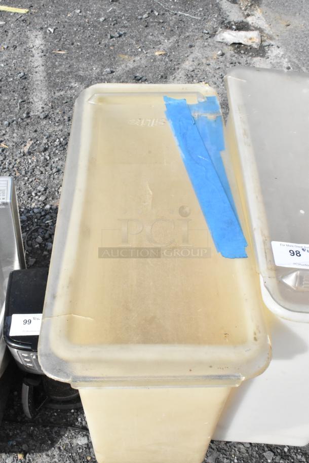 White poly ingredient bin on commercial casters, worn condition, blue tape marking on lid, auction tags visible.