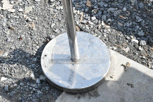 Chrome metal stand with a round base, outdoor setting, showing wear. Ideal for retail or events.