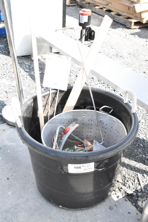 Black poly bin with mixed contents, including a metal steam stock pot, tools, and wooden pieces. Label marked "108" visible.