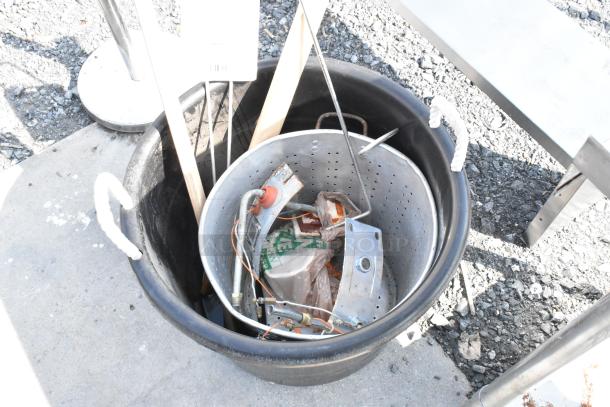 Black poly bin with rope handles containing a perforated steam stock pot, wooden tools, and assorted metal parts.