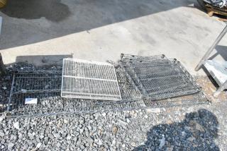 Lot of 6 various wire shelves, mixed sizes and colors, stacked outdoors on gravel. Some rust and wear visible.