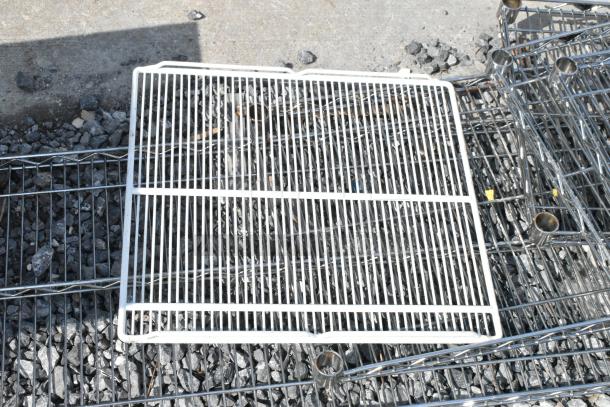 Lot of 6 various wire shelves, mixed sizes and colors, on rocky outdoor surface. Suitable for storage or display.