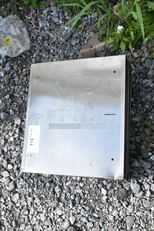 Stainless steel metal bin with visible wear. Auction tag reads "113." Located outdoors on gravel.