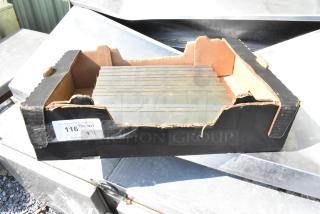 11 metal pieces in a cardboard box. Box labeled "116 1/2 QTY XII" from PCI Auctions. Metal pieces are flat and rectangular.