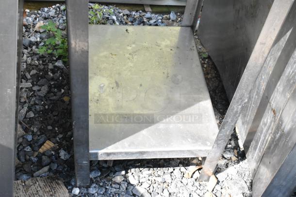 Metal table with sturdy construction and an under shelf. Shows signs of outdoor wear. Ideal for industrial use.