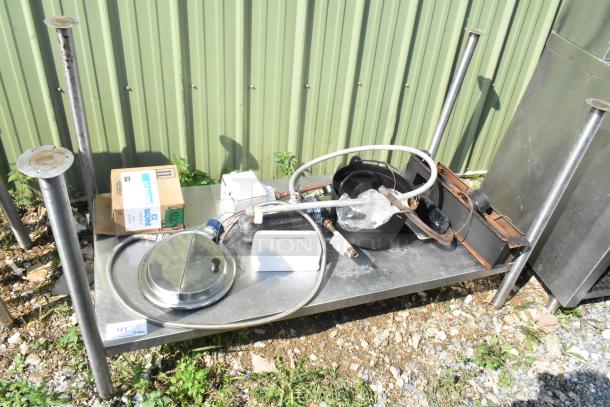 Metal under shelf with legs containing assorted plumbing and mechanical parts, includes a box labeled "Ice Machine," set outdoors.