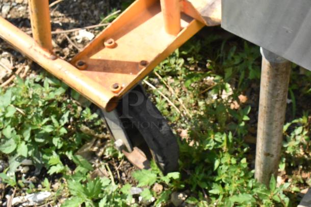 Metal cart on commercial casters, featuring a sturdy orange frame. Casters appear in used condition, suitable for heavy-duty use.