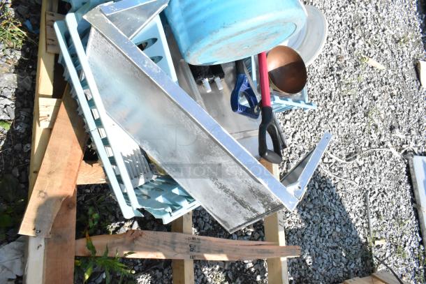 Pallet of items including snow shovels, a blue poly bucket, and a metal shelf, mixed condition, outdoors on gravel.