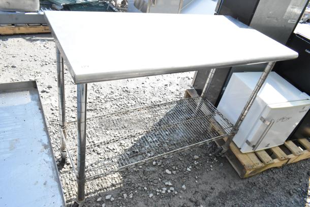 Stainless steel table with wire under shelf, on commercial casters. Outdoor setting, sturdy and functional design.