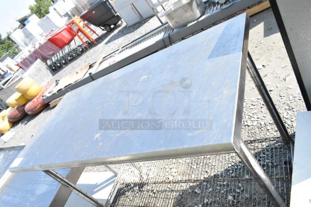 Stainless steel table with wire under shelf on commercial casters, suitable for kitchen use. Shows signs of light wear.