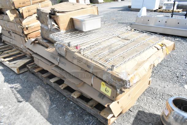 Stack of new, scratch and dent commercial kitchen items on pallets, including Steelton and Regency stainless steel stands and tables.