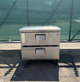 Commercial stainless steel 2-drawer undercounter refrigerator on wheels, used condition, with manufacturer logo and label tag visible.