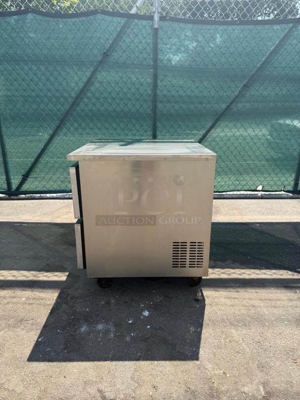 Commercial stainless steel 2-drawer undercounter refrigerator, shown in outdoor setting, appears in good condition.