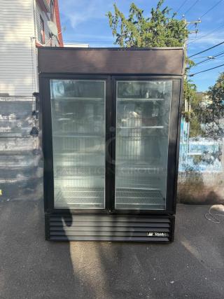 True GDM-49-HC~TSL01 glass door merchandiser, black, double left hinge doors, shelves inside, outdoor setting, clear glass.