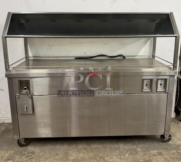 Stainless steel hot food merchandiser on wheels, with glass display, PCI Auction Group label, and power switches, good condition.