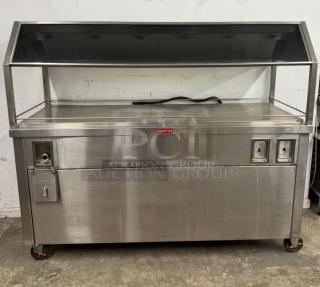 Stainless steel hot food merchandiser on wheels, with glass display, PCI Auction Group label, and power switches, good condition.