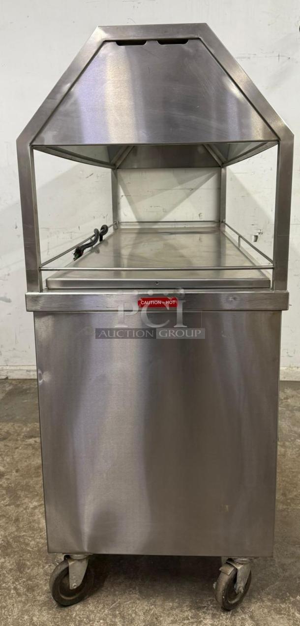 Stainless steel hot food merchandiser with tempered glass sides, labeled "Caution – Hot," on wheels, used condition.