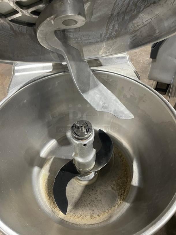 Hobart commercial electric vertical chopper with stainless steel tilting bowl and cover, shown with blades. Mounted on legs and casters.