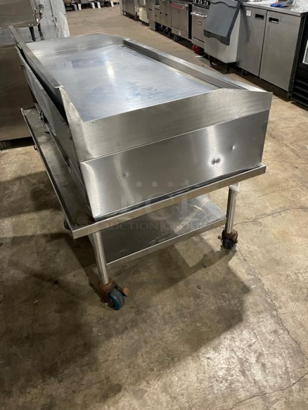 Commercial stainless steel gas countertop flat griddle with thermostatic controls, back and side splash, undershelf, and casters.