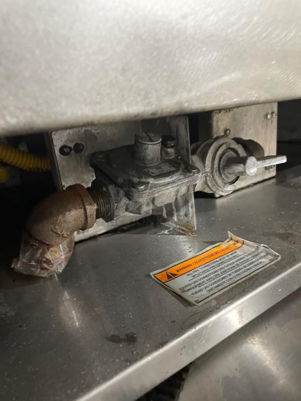 Commercial stainless steel natural gas flat griddle with thermostatic controls, back and side splash. Includes single undershelf equipment stand on casters. Warning label visible.