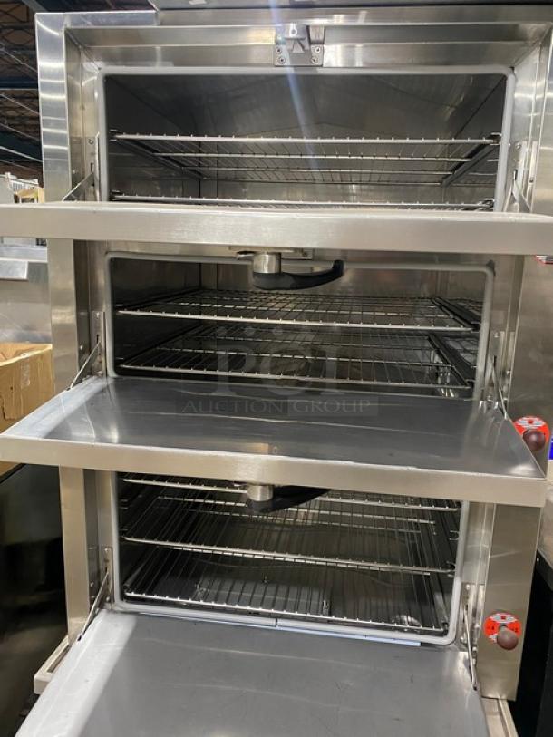 Commercial stainless steel 3-compartment steamer cabinet with individual controls, wired oven racks, on legs, natural gas powered.