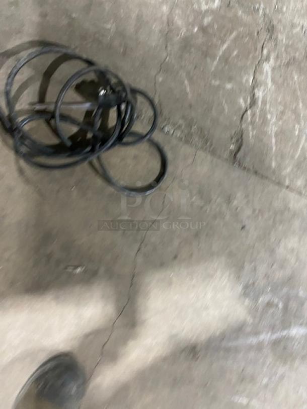 A tangled black power cord on a concrete floor.