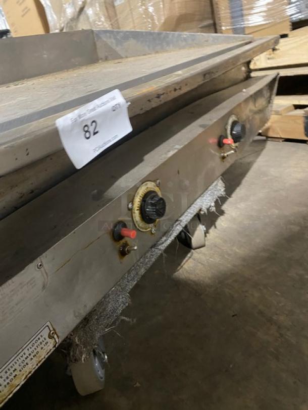 Commercial stainless steel gas flat griddle with thermostatic controls, back, and side splash. Slight wear visible.