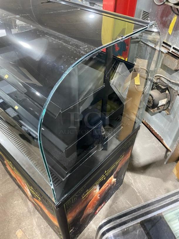 Commercial black refrigerated bakery display case, curved glass, multi-tier shelves, excellent condition. Ideal for desserts.