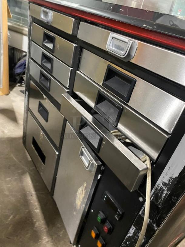 Commercial black curved glass refrigerated bakery display case, multi-tier, stainless steel drawers, moderate wear.
